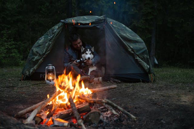 A man happily camping with its siberian husky dog.