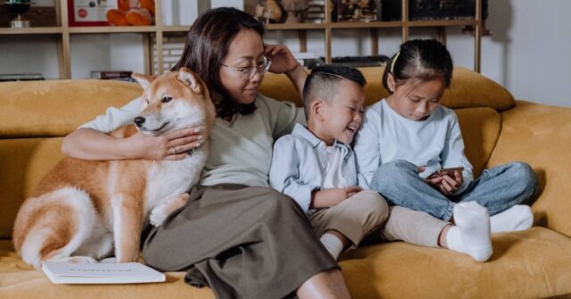 Mom sitting on a sofa with her two kids and thei dog.