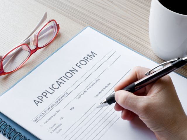 Person holding a pen about to complete an application form with glasses and coffee cup on the table.