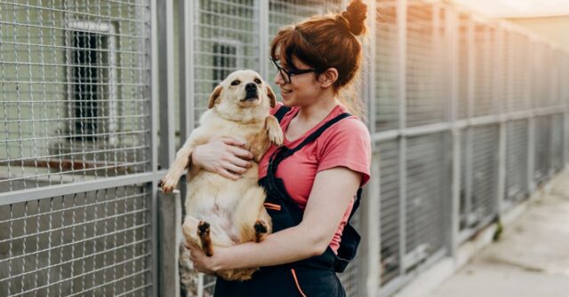 Woman holding a dog in her hands at a rescue shelter with cages behind them.